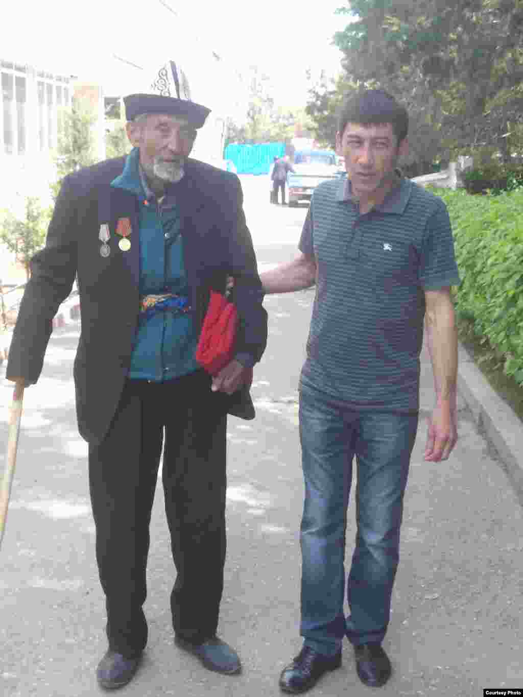 Yosh yigit mehnat faxriysining qo'lidan ushlab yurishiga yordamlashmoqda.