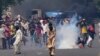 FILE - Supporters of Pakistan's former Prime Minister Imran Khan remove tear gas shell fired by police to disperse them during a protest in Lahore, Pakistan, May 10, 2023.