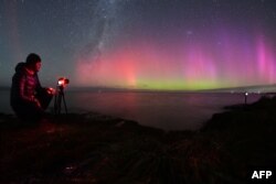 A photographer takes pictures of the Aurora Australis, also known as the Southern Lights, as it glows on the horizon over waters of Lake Ellesmere on the outskirts of Christchurch, New Zealand, April 24, 2023.
