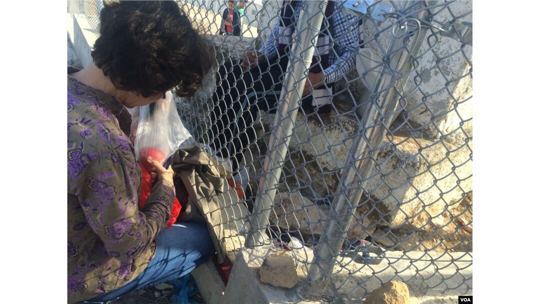 A local woman passes fruit and sweets to a young man trapped inside the refugee camp in Lesbos, Greece, April 1, 2016. (H. Murdock/VOA)