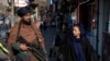 FILE - A Taliban fighter stands guard as a woman walks past in Kabul, Afghanistan, Dec. 26, 2022. 