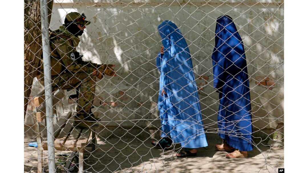 FILE - A Taliban fighter stands guard as two women enter the government passport office in Kabul, April 27, 2022. Afghanistan's Taliban leadership has ordered all Afghan women to wear the all-covering burqa in public.
