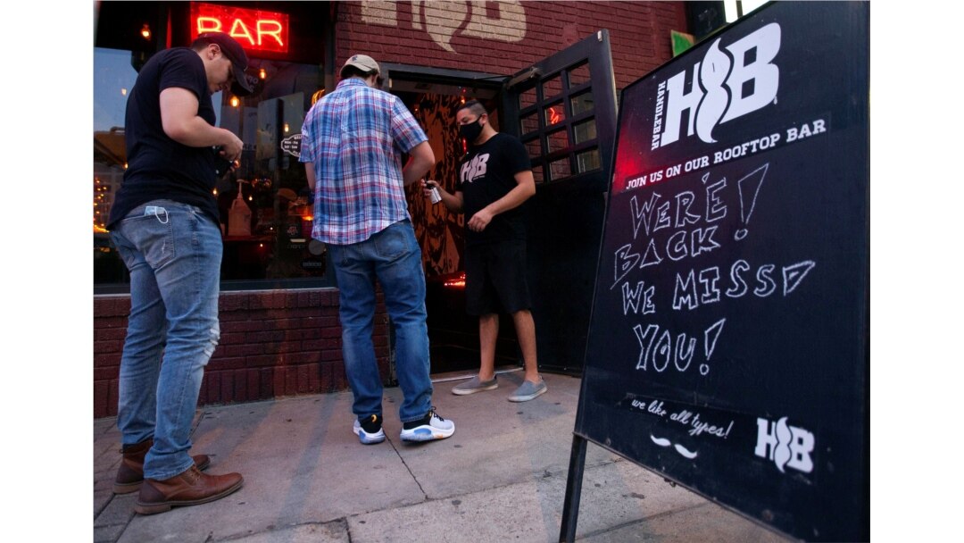 FILE - Handlebar bouncer, Mando Cuadros, sprays down a guest's hands with hand sanitizer on the first night that bars reopen after they were shut down to stop the spread of the coronavirus disease (COVID-19) in Austin, Texas, May 22, 2020.