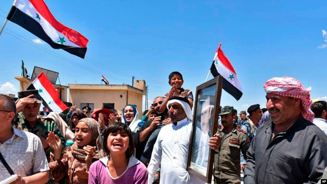 In this photo released by the Syrian official news agency SANA, Syrians welcome government forces and police entering their village with a portrait of President Assad, national flags, and patriotic slogans, in northern countryside of Homs province, May 14, 2018.