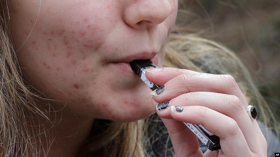 FILE - A high school student uses a vaping device near a school campus in Cambridge, Mass.