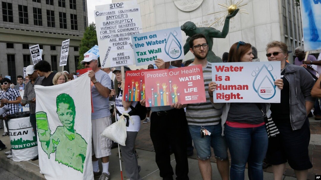 FILE - People stand outside Detroit City Hall, protesting thousands of residential water-service shutoffs by Detroit's water department, during a rally in Detroit, Thursday, July 24, 2014.