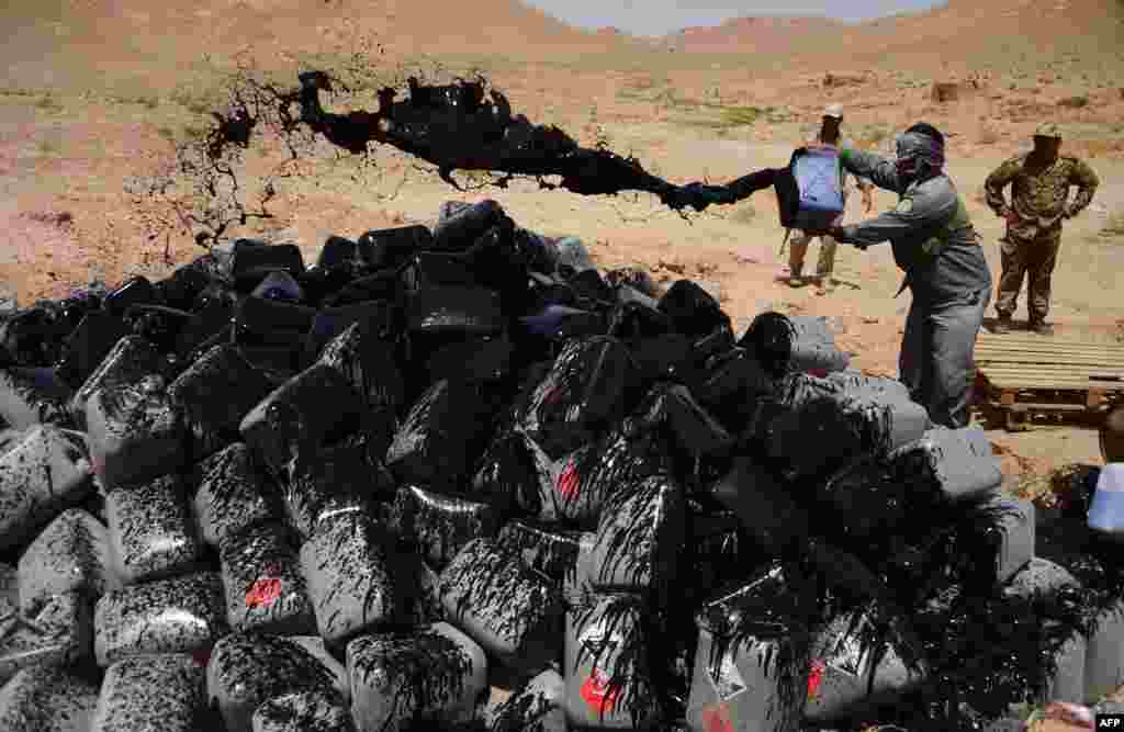 A policeman pours fuel over jerry cans containing confiscated acetic acid before setting it alight, on the outskirts of Herat, Afghanistan.