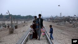 A homeless Iraqi family walks along railway tracks toward their hut, outside Baghdad, Iraq, Feb. 12, 2018. 