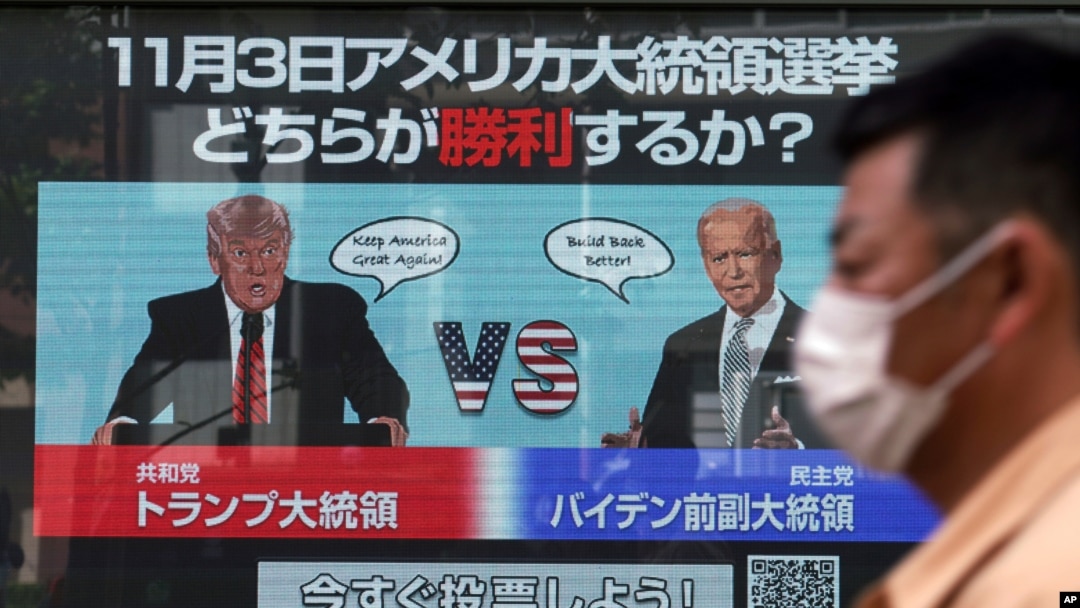 FILE - A man walks past a screen showing illustrations of President Donald Trump, left, and former Vice President Joe Biden for an online voting to predict the winner in the U.S. presidential election, in Tokyo, Oct. 26, 2020. 