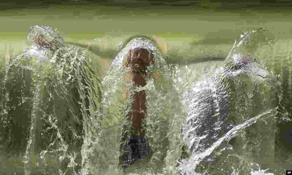 A man refreshes himself underneath a small waterfall in the English Garden in Munich, Germany.