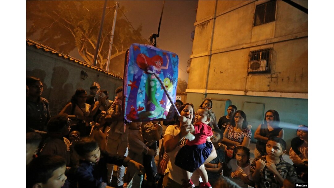 FILE - A woman holds a child as they get ready to hit a pinata at a birthday party celebration in Caracas, Venezuela, April 13, 2019.