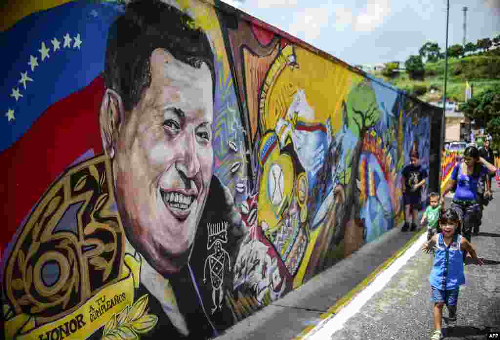 Children walk by a mural depicting late Venezuelan president Hugo Chavez at the "23 de Enero" neighborhood in Caracas near the "Cuartel de la Montaña" museum where his body rests, on the 63rd anniversary of his birth.