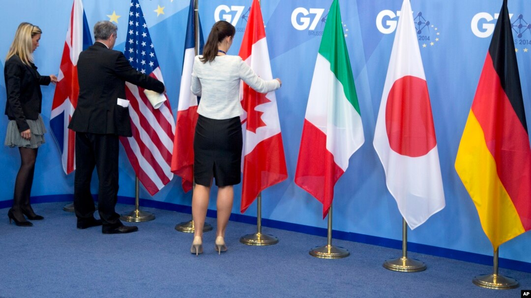Workers adjust the flags of a Group of Seven meeting in Brussels, Belgium, June 5, 2014. G-7 foreign ministers are meeting Monday and Tuesday in Tuscany, Italy.