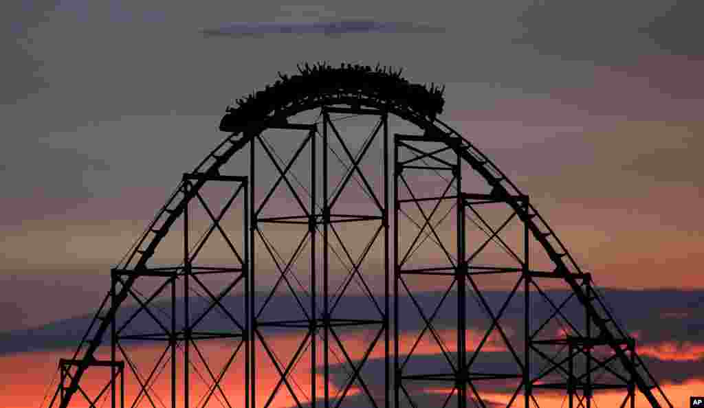 People ride a roller coaster at dusk at Worlds of Fun amusement park, July 3, 2017, in Kansas City, Missouri.