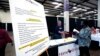 A list of benefits flanks Jon Stembridge, center, a human resource and safety manager with HomeStretch, a domestic manufacturer of upholstered reclining furniture, as he welcomes a potential applicant to his company's recruiting booth, Miss., Oct. 12, 2021. 
