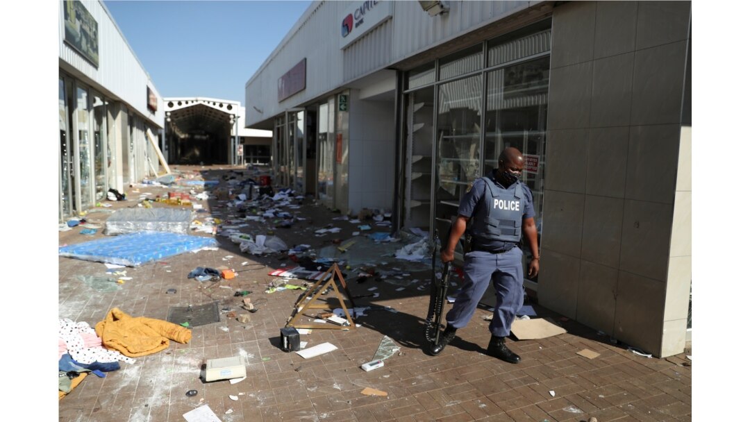 FILE - A police officer stands on the street, next to vandalized and looted stores, as protests continue following imprisonment of former South Africa President Jacob Zuma, in Katlehong, South Africa, July 12, 2021.