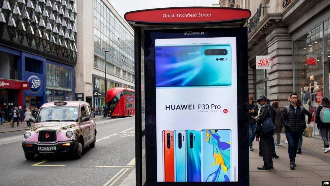 FILE - Pedestrians walk past a Huawei ad at a bus stop in central London, April 29, 2019.