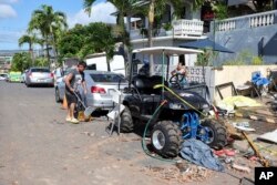 Neighbors clean up debris near the home where a New Year's Eve fireworks explosion killed and injured people, Jan. 1, 2025, in Honolulu.