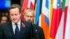 FILE - British Prime Minister David Cameron (L) walks past EU member state flags as he departs from an EU summit in Brussels Oct. 24, 2014.
