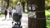 A woman pushes a pram past a giant mask and eye display stuck to a tree in Melbourne, May 8, 2020, as Australia's government unveiled a three-stage plan to get the economy back to a new normal by the end of July. 