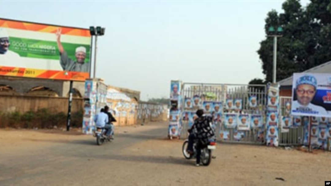 Members of the Party Loyalists drive their motocycles outside the entrance of a park in front of posters featuring Nigeria's opposition leader Mohammadu Buhari (R) and Nigeria's President Goodluck Jonathan and his Vice President Namadi Sambo (L) in Kad