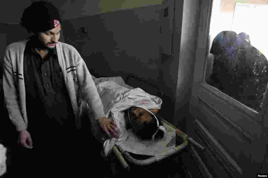 A woman looks through a window while a man who was wounded in a bomb attack at Fauji Market lies at the Hayatabad hospital in Peshawar, Pakistan, December 17, 2012.