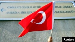FILE - A person holds a Turkish flag under a sign on the U.S. Consulate in Istanbul.