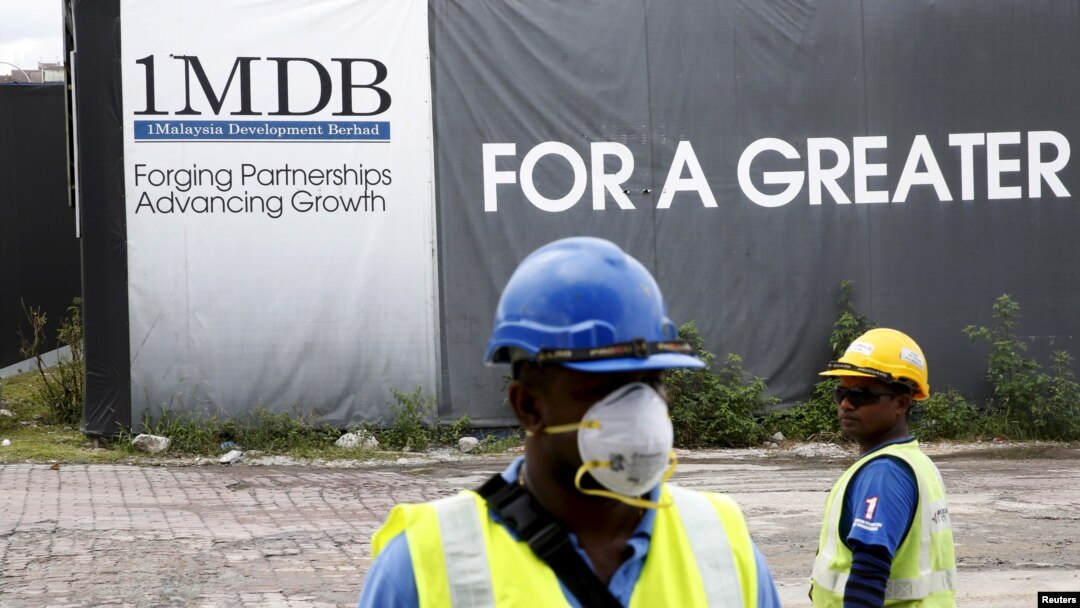 FILE - Construction workers stand in front of a 1Malaysia Development Berhad (1MDB) billboard at the Tun Razak Exchange development in Kuala Lumpur, Malaysia.