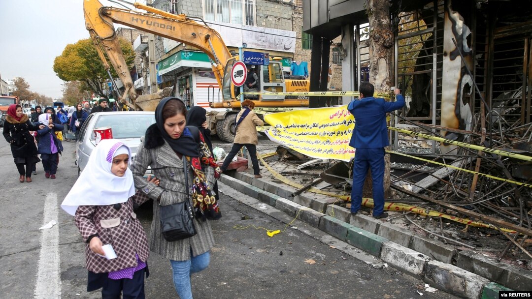 FILE - People walk near a burned bank after protests against increased fuel prices, in Tehran, Iran, Nov. 20, 2019. 