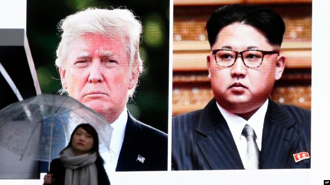 A woman walks by a huge screen showing U.S. President Donald Trump, left, and North Korea's leader Kim Jong Un, in Tokyo, March 9, 2018.