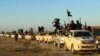 FILE - In this undated file photo released by a militant website, which has been verified and is consistent with other AP reporting, militants of the Islamic State group hold up their weapons and wave flags on their vehicles in a convoy on a road leading leading to Iraq, while riding in Raqqa, Syria. 