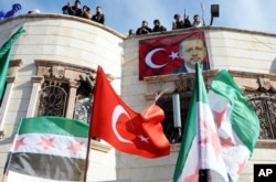 FILE - Turkey-backed Free Syrian Army, FSA, fighters stand on the roof of a building with a poster of Turkey's President Recep Tayyip Erdogan hanging on it in the Syrian town of Azez near the border with Turkey, Jan. 19, 2018.
