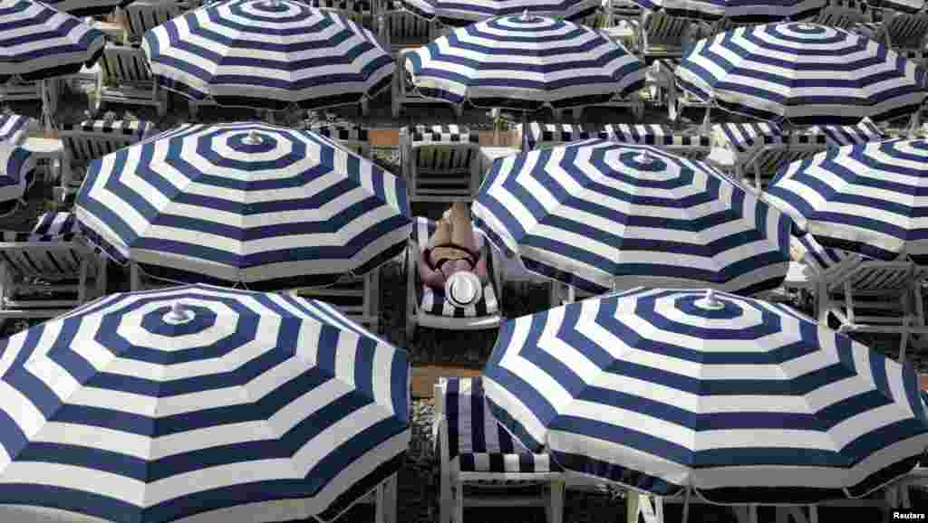 A tourist enjoys the sun on a beach along the Promenade Des Anglais during a sunny summer day in Nice, France.