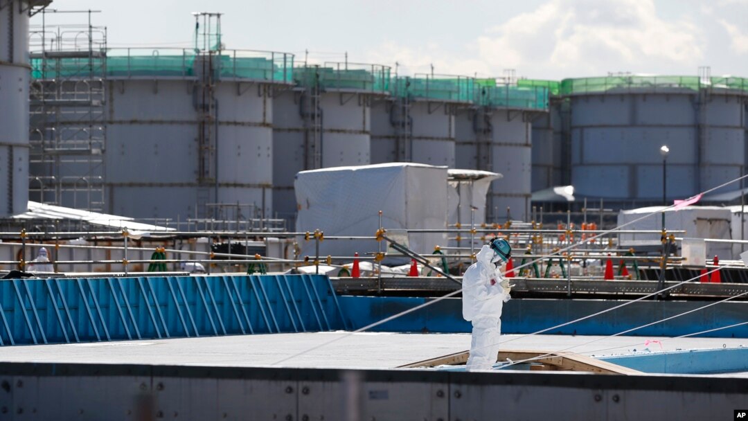FILE - A worker, wearing protective suits and masks, takes notes in front of storage tanks for radioactive water at the tsunami-crippled Fukushima Dai-ichi nuclear power plant, operated by Tokyo Electric Power Co. (TEPCO), in Okuma, Fukushima Prefecture, northeastern Japan. To dump or not to dump a little-discussed substance is the question brewing in Japan as it grapples with the aftermath of the nuclear catastrophe in Fukushima five years ago. The substance is tritium, Feb. 10, 2016.