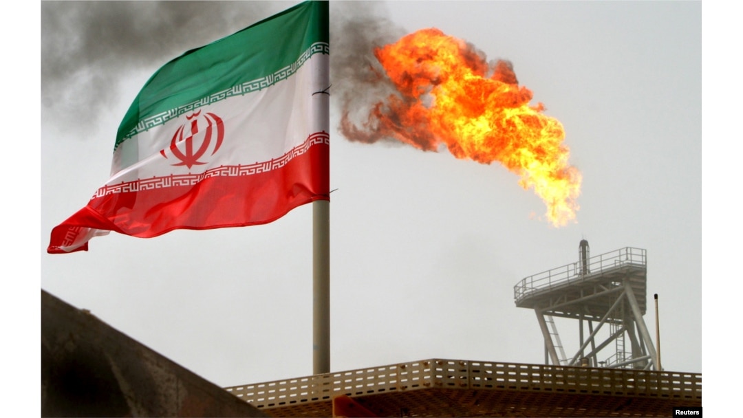 FILE - A gas flare on an oil production platform in the Soroush oil fields is seen alongside an Iranian flag in the Persian Gulf, Iran, July 25, 2005.