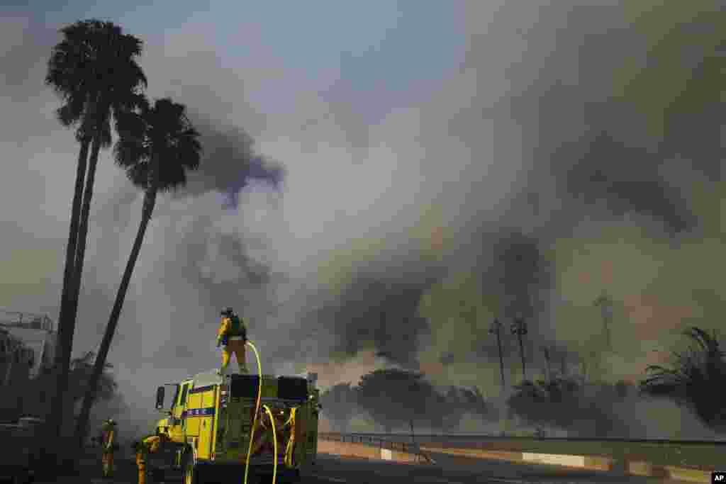 Firefighters battle a wildfire as smoke rises from burning palm trees at Faria State Beach in Ventura, California, Dec. 7, 2017.