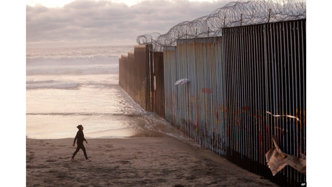 A woman walks on the beach, Jan. 9, 2019, next to the border wall topped with razor wire in Tijuana, Mexico.