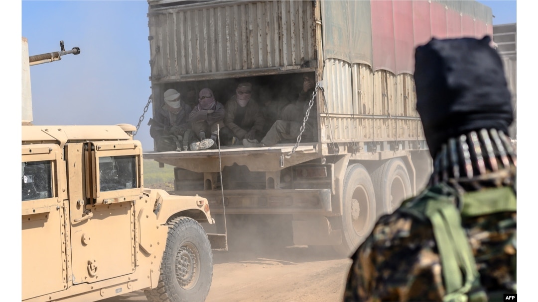 A truck carries men identified as Islamic State group fighters who surrendered to Kurdish-led Syrian Democratic Forces (SDF) as they are transported out of IS's last holdout of Baghuz, Syria, Feb. 20, 2019.
