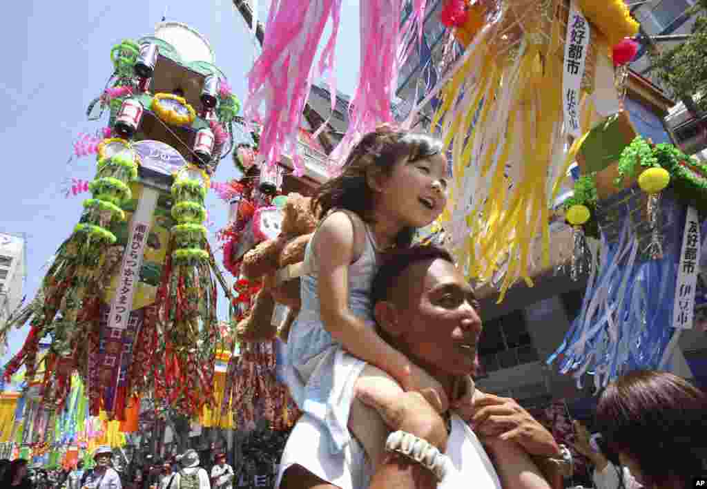 A girl is carried on her father's shoulder as people walk under colorful paper streamers decorated at a shopping street to celebrate the Tanabata Star Festival in Hiratsuka, near Tokyo. People celebrate the festival by writing wishes on strips of paper and hanging them under bamboo trees.