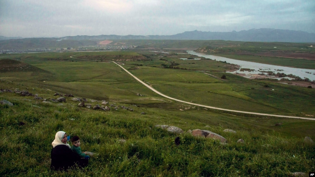 FILE - In this file photo dated Wednesday, May 1, 2019, a woman and child sit on a hill overlooking the Euphrates River as families picnic on May Day, in Derik, Syria. 