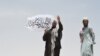 Một người đứng ở biên giới trên phần đất Afghanistan, cầm cờ Taliban.