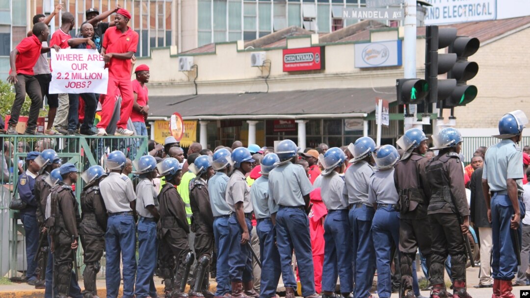 Zimbabwean police officers keep an eye on opposition party supporters as they prepare to march during a protest aimed at President Robert Mugabe in Harare, March, 14, 2016.