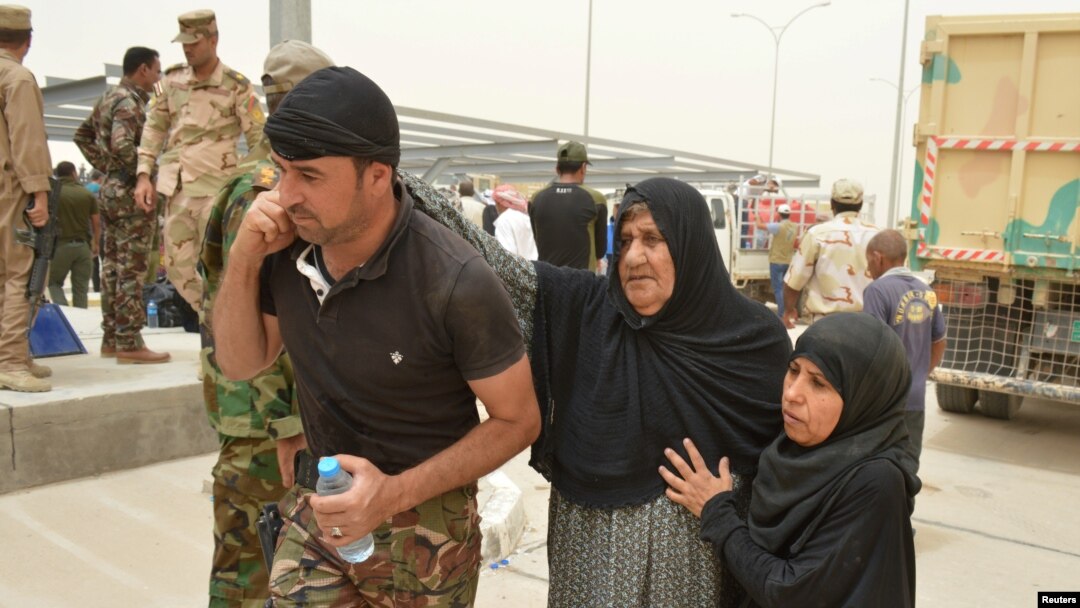 A tribal fighter helps civilians on the outskirts of Falluja, Iraq, June 18, 2016. Iraqi government-run camps struggled to shelter people fleeing Falluja, as the military battled Islamic State militants in the city's northern districts.