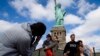Tourists pose for photographs in front of the Statue of Liberty in New York Harbor in New York. The Statue of Liberty reopened to the public after the state of New York agreed to shoulder the costs of running the site during the partial federal government