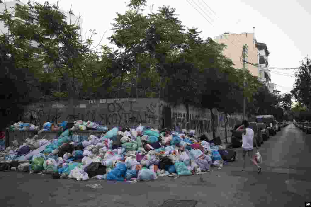 A woman walks past a pile of trash as a sign on the wall reads in Greek "No garbage" in the Kaminia neighborhood of Piraeus, near Athens. Greece's municipal garbage collectors are on a 14-day protest that has left mounds of festering refuse piled up across Athens amid high summer temperatures.