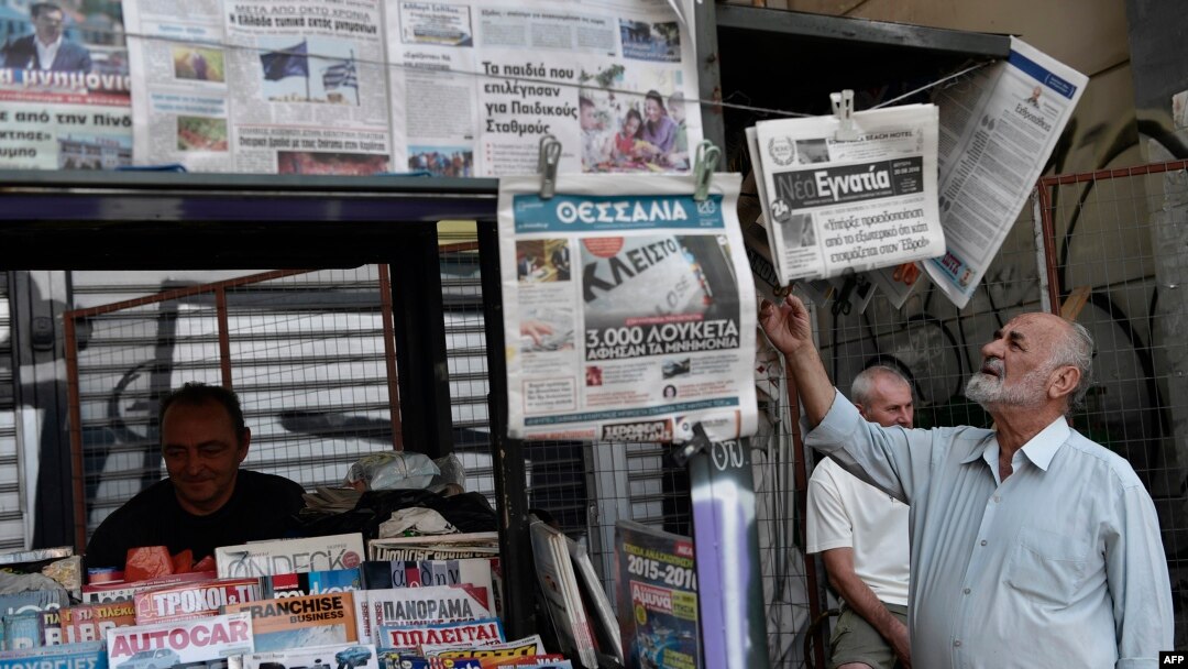 FILE - A man reads newspapers' headlines in central Athens, Aug. 21, 2018, as the country ended eight years of painful bailouts. On Monday, eurozone ministers delayed granting Greece debt relief because the government failed to implement reforms promised during the bailout.
