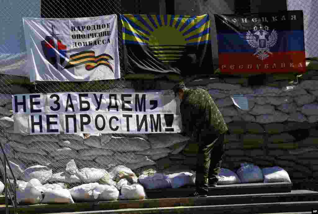 Rossiyaparast qurollangan shaxs sharqiy Ukrainaning Slavyansk shahridagi ma'muriyat binosi oldiga "Unutmaymiz va kechirmaymiz" deb yozilgan plakatni osmoqda.