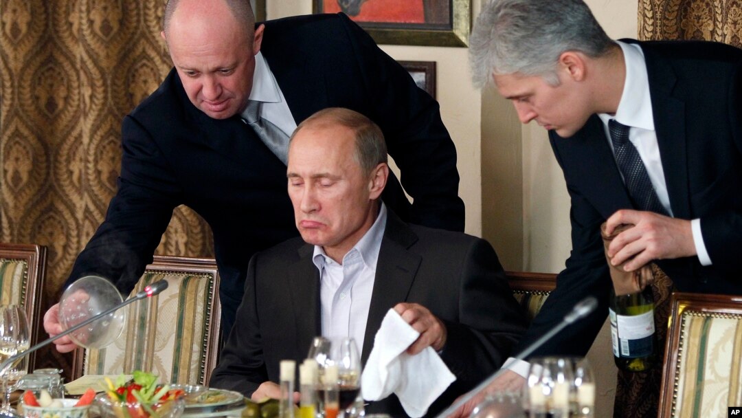 FILE - In this Nov. 11, 2011, photo, businessman Yevgeny Prigozhin, left, serves food to Russian Prime Minister Vladimir Putin, center, during dinner at Prigozhin's restaurant outside Moscow. 