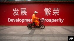 一名北京市清洁工人骑车经过市中心街头张贴的发展与繁荣的标语牌。（2015年7月15日）