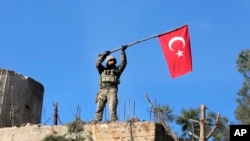 FILE - A soldier waves a Turkish flag as Turkish troops secure Bursayah hill, which separates the Kurdish-held enclave of Afrin from the Turkey-controlled town of Azaz, Syria, Jan. 28, 2018. 